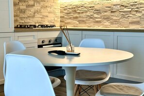 A modern kitchen with a round table, white chairs, and a stone backsplash.
