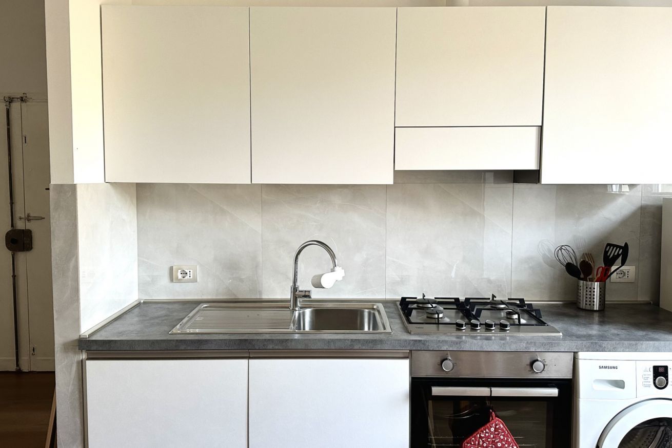 A kitchen with white cabinets, a stainless steel sink, a gas stove, and a built-in washing machine.