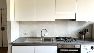 A kitchen with white cabinets, a stainless steel sink, a gas stove, and a built-in washing machine.