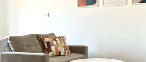 A living room with a grey sofa, a patterned throw pillow, a round white table, and abstract art on the wall.