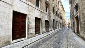 A narrow cobblestone street flanked by historic buildings with closed shutters and a visible green sign. - A39 - Ancona, comfortable three-room apartment in the historic center (Ancona)