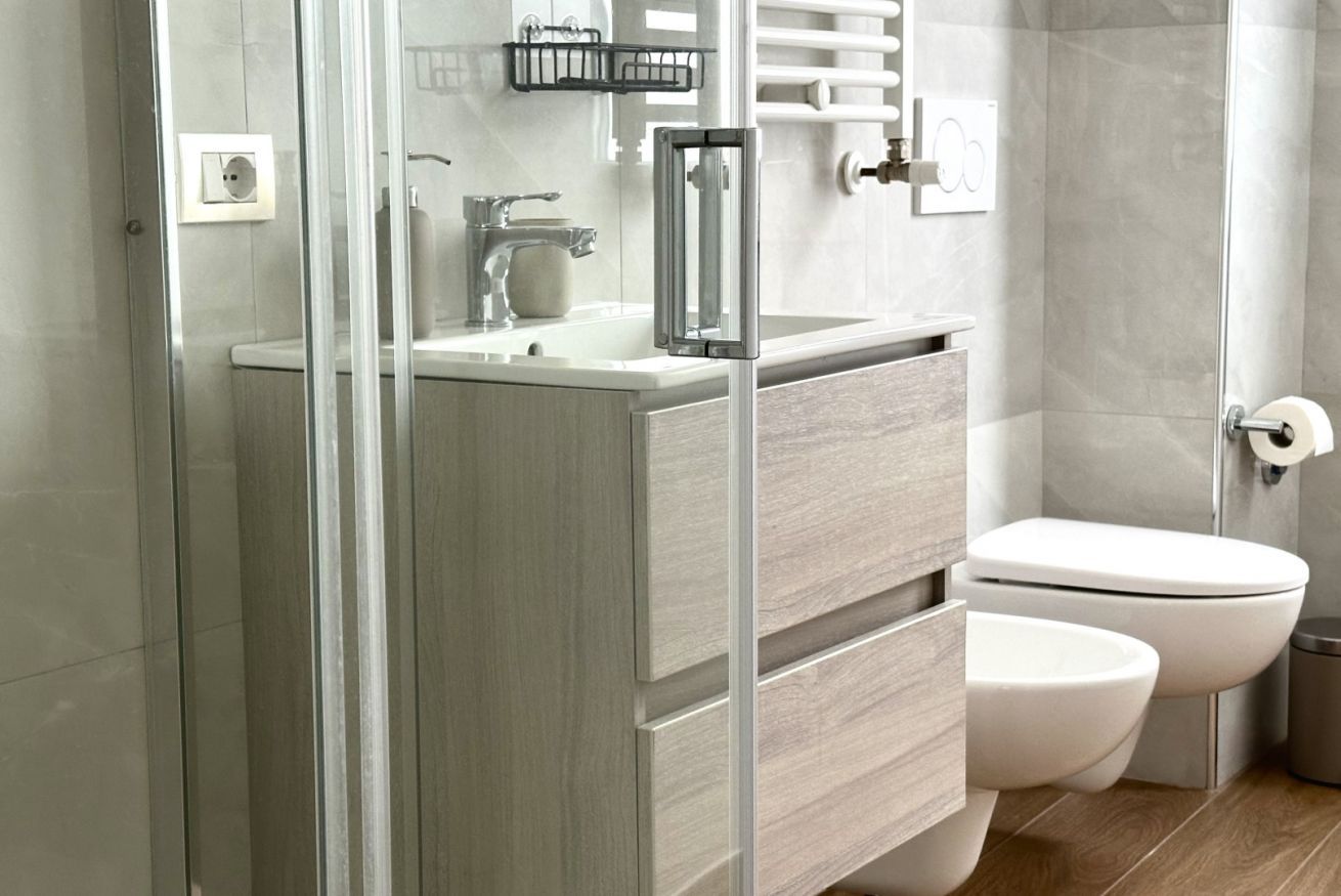 A modern bathroom with a glass shower enclosure, a white sink, and a toilet.