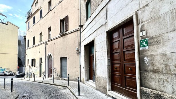 A cobblestone street with a building featuring a large wooden door and a green sign indicating a public area. - A39 - Ancona, comfortable three-room apartment in the historic center (Ancona)