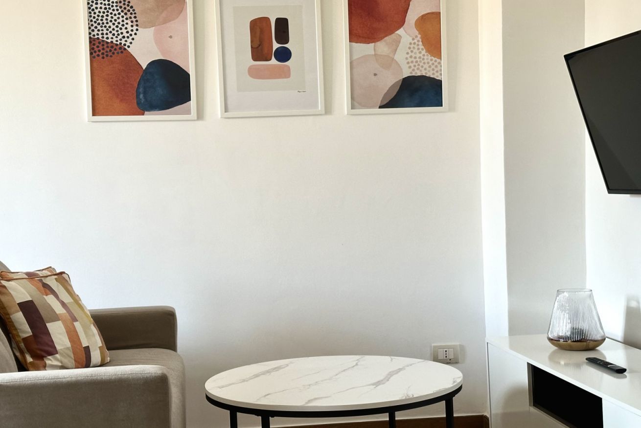 A living room with a round table, a sofa, abstract art on the wall, and a TV mounted on the wall.