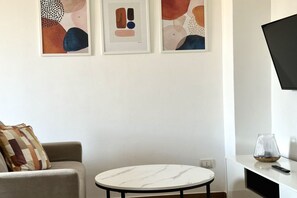 A living room with a round table, a sofa, abstract art on the wall, and a TV mounted on the wall.