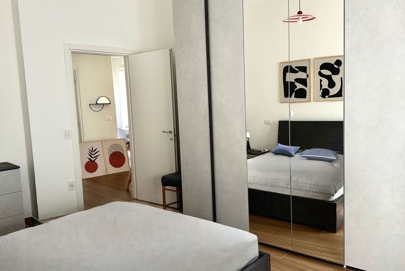 Ein Schlafzimmer mit einem Bett, einem Spiegel und einer Tür zu einem anderen Raum.