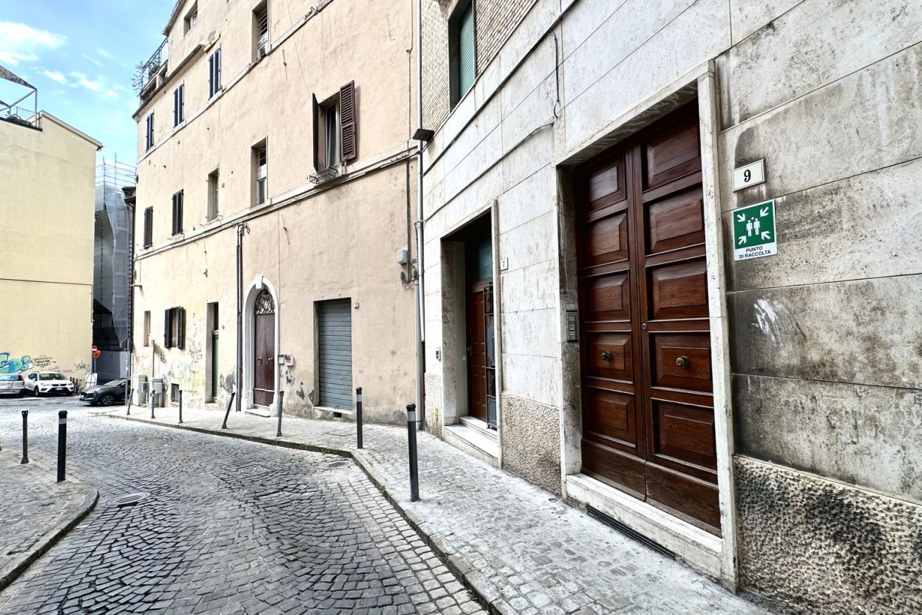 Eine Kopfsteinpflasterstraße mit einem Gebäude, das eine große Holztür und ein grünes Schild mit der Bezeichnung für einen öffentlichen Bereich aufweist.