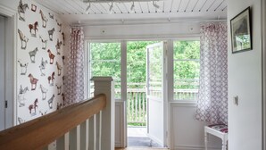 A room with a wooden staircase, a door leading outside, and a window with curtains.