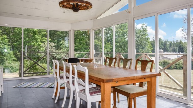 A dining area with a wooden table and white chairs, large windows offering a view of trees and a wooden deck outside.