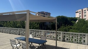 An outdoor patio with a table and chairs, a pergola, and a view of buildings and trees. - M398 - Marcelli, three-room apartment with terrace in residence with pool (Marcelli)