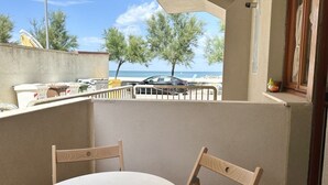 A balcony with a round table and two chairs, overlooking a beach and parked cars. - SE106 - Senigallia, new two-room apartment facing the sea (Cesano)
