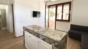 A modern kitchen with a glass-top island, a flat-screen TV, and a sliding glass door to the outside. - SE106 - Senigallia, new two-room apartment facing the sea (Cesano)