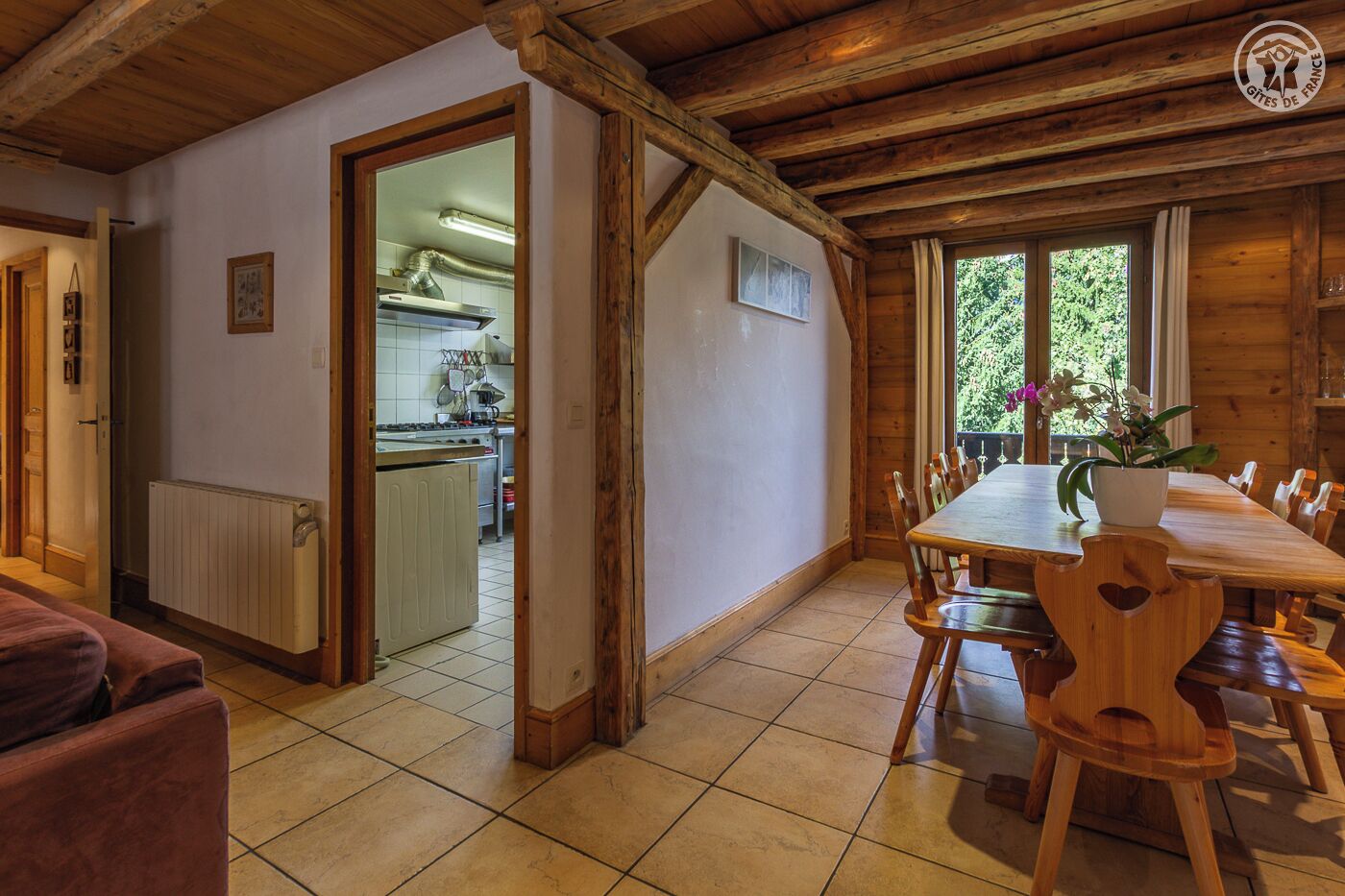 Un intérieur en bois comprenant une table à manger, des chaises, un coin cuisine et une vue sur la verdure à l’extérieur.
