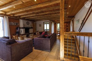 Un intérieur rustique avec des poutres apparentes, un escalier doté d’une rampe en fer forgé et un coin salon confortable avec des canapés.