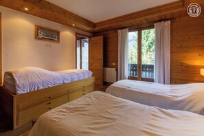 Una habitación con dos camas, paredes de madera, un ventanal con cortinas y un radiador.