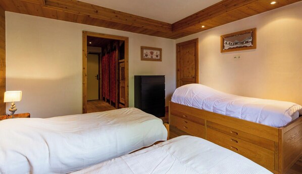 Une chambre avec deux lits, un plafond en bois, une porte avec des rideaux rouges, un tableau accroché au mur et une table de chevet avec une lampe.