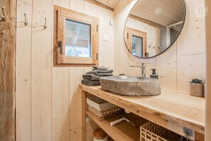 Een houten badkamer met een stenen wasbak, een raam en een spiegel.