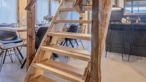 Un escalier en bois rustique, avec un coin repas et une cuisine en arrière-plan.