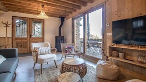 Un salon chaleureux avec des poutres en bois, un grand téléviseur, des meubles en osier et une cheminée en pierre.