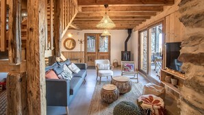 Un intérieur rustique avec des poutres apparentes, un coin salon confortable avec un canapé et des fauteuils, une cheminée et de grandes fenêtres offrant une vue imprenable.