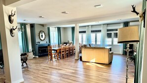 A spacious living area with a wooden floor, a sofa, a dining table with chairs, and a fireplace. - Casa Sierra Morena. Lince (AN)