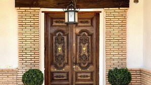 A wooden double door with intricate carvings, flanked by two large terracotta pots with topiary plants, under a hanging lantern. - Casa Sierra Morena. Lince (AN)