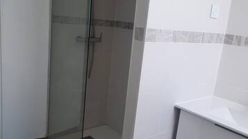 Ein Badezimmer mit einer gläsernen Dusche, einem weißen Waschbecken und einer Holzbadematte auf dem Boden.