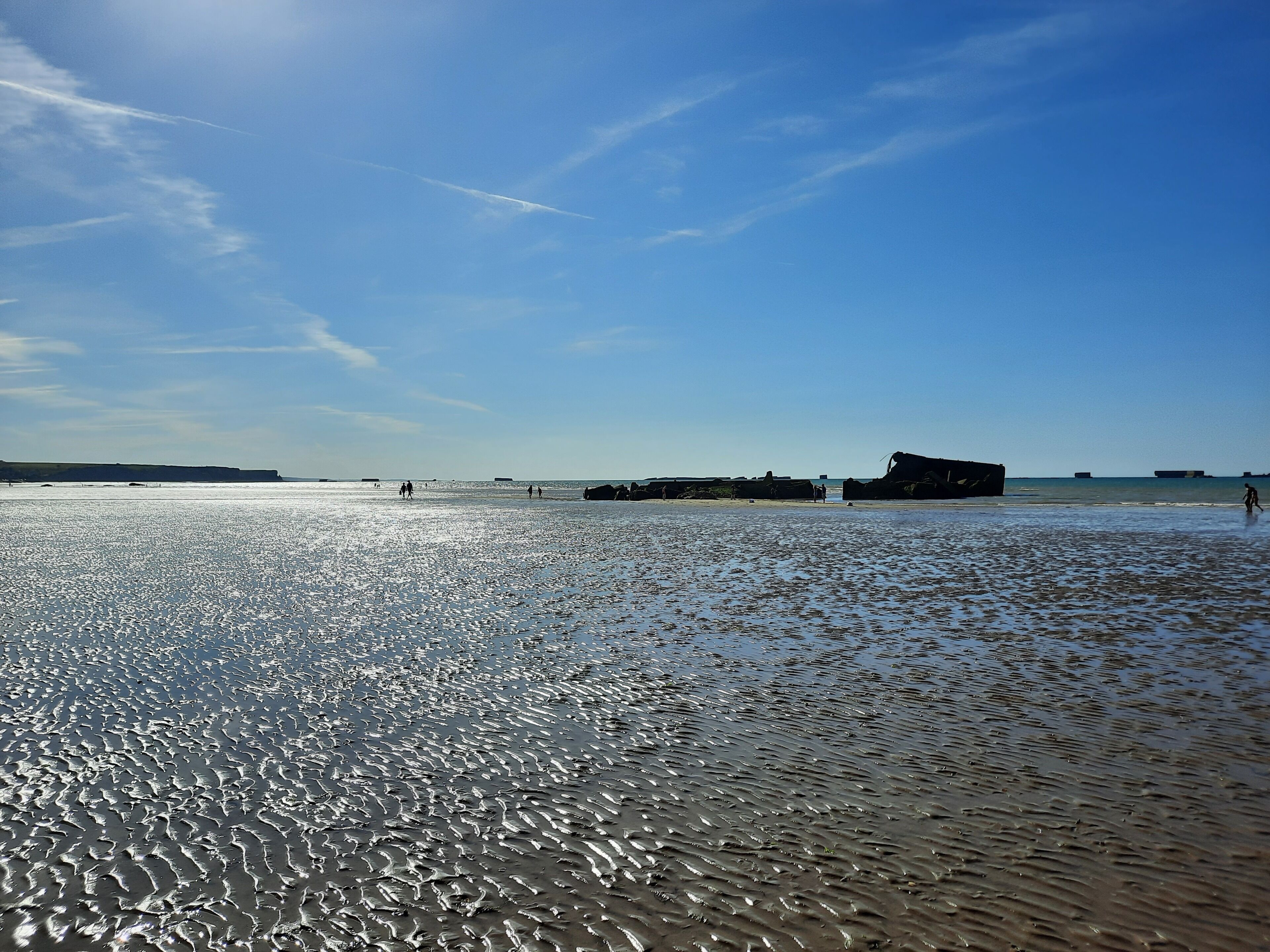 Ein Strand mit blauem Himmel, ruhiger See und einer großen Felsformation in der Ferne.