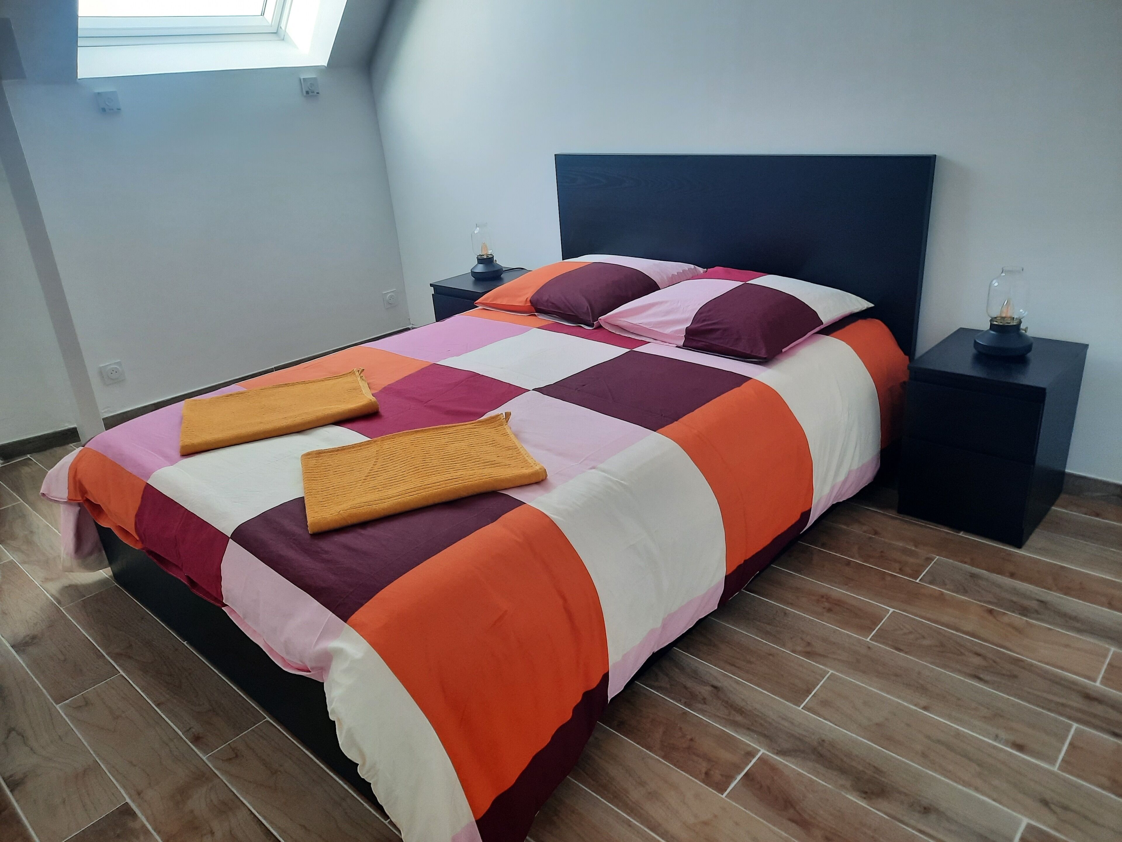 Un letto rifatto con cura, un patchwork colorato, due comodini con lampade e una finestra sopra il letto.