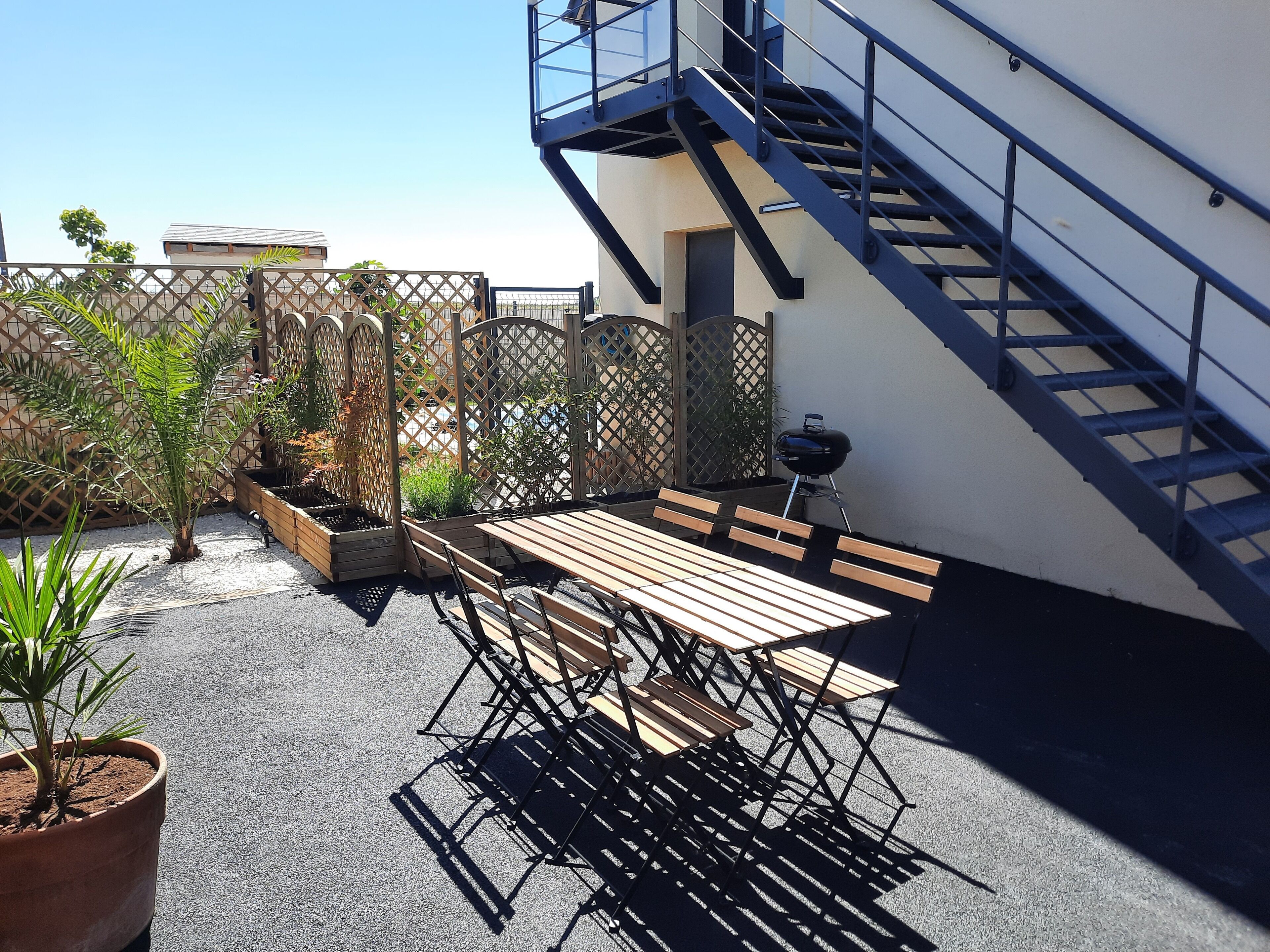 An outdoor patio with a wooden table and chairs, a grill, and a staircase leading to an upper level.