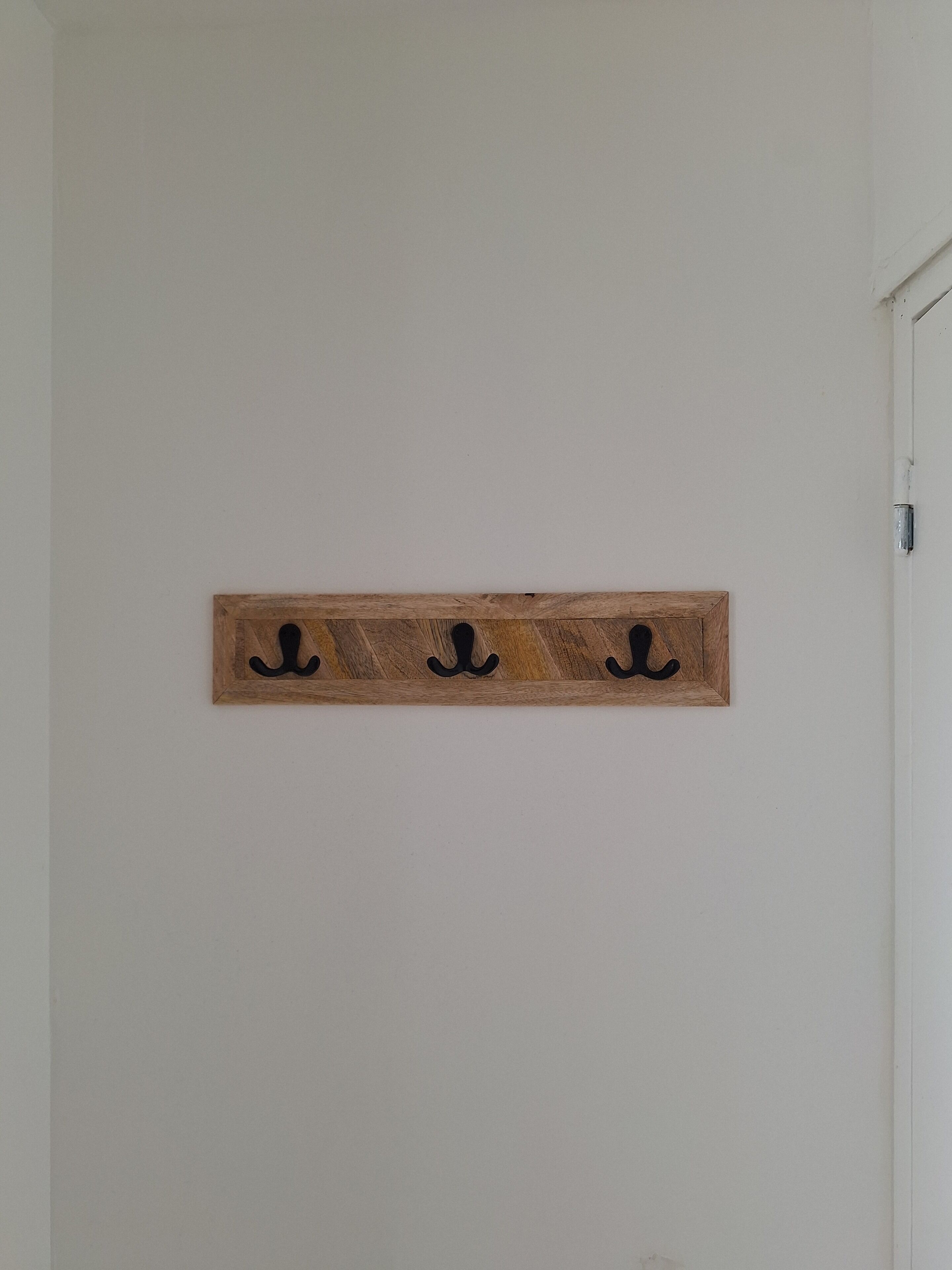 Un adorno de madera fijado a la pared con tres ganchos negros.