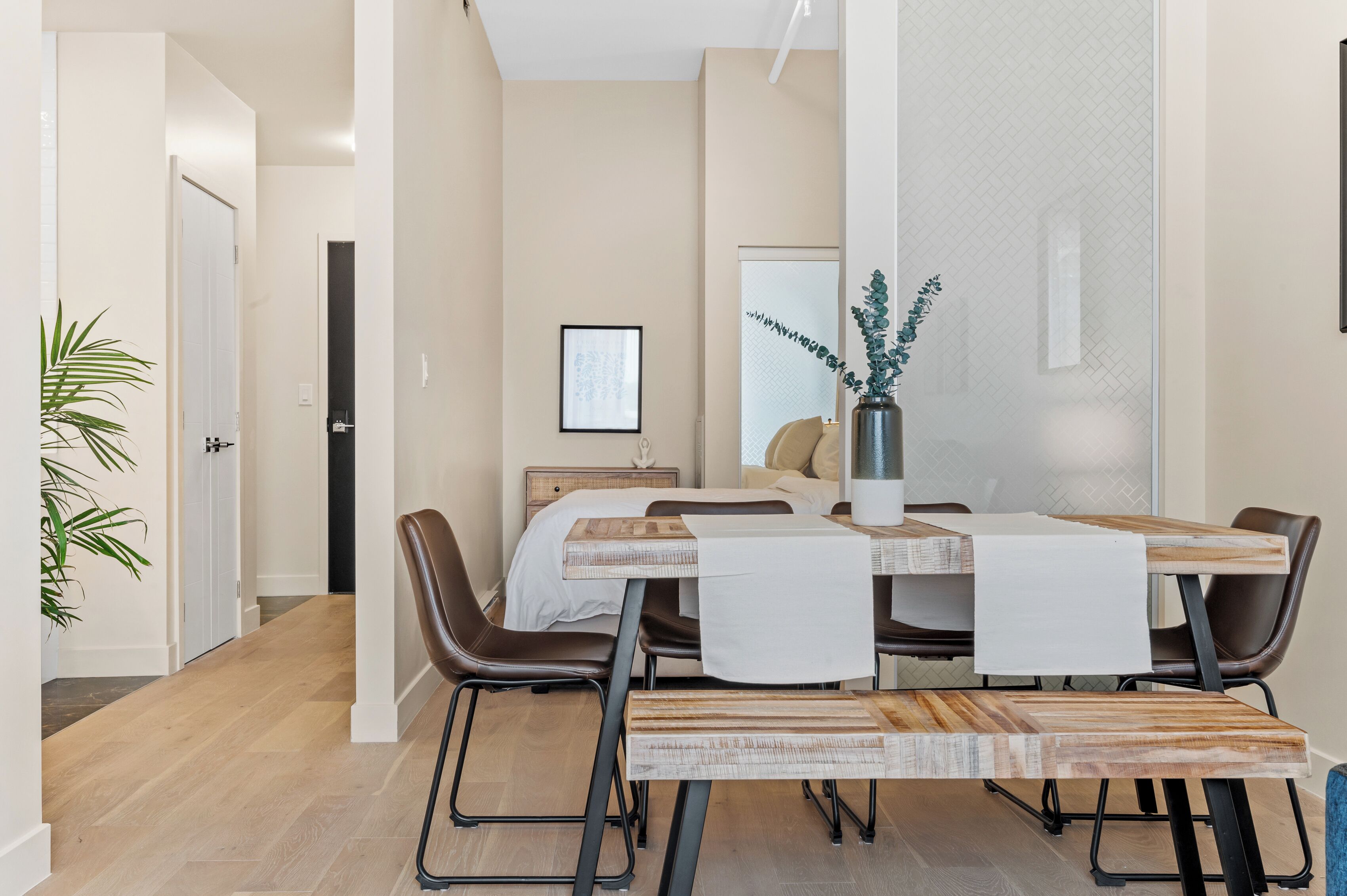 A modern dining area with a wooden table and chairs, a vase with greenery, and a framed picture on the wall.