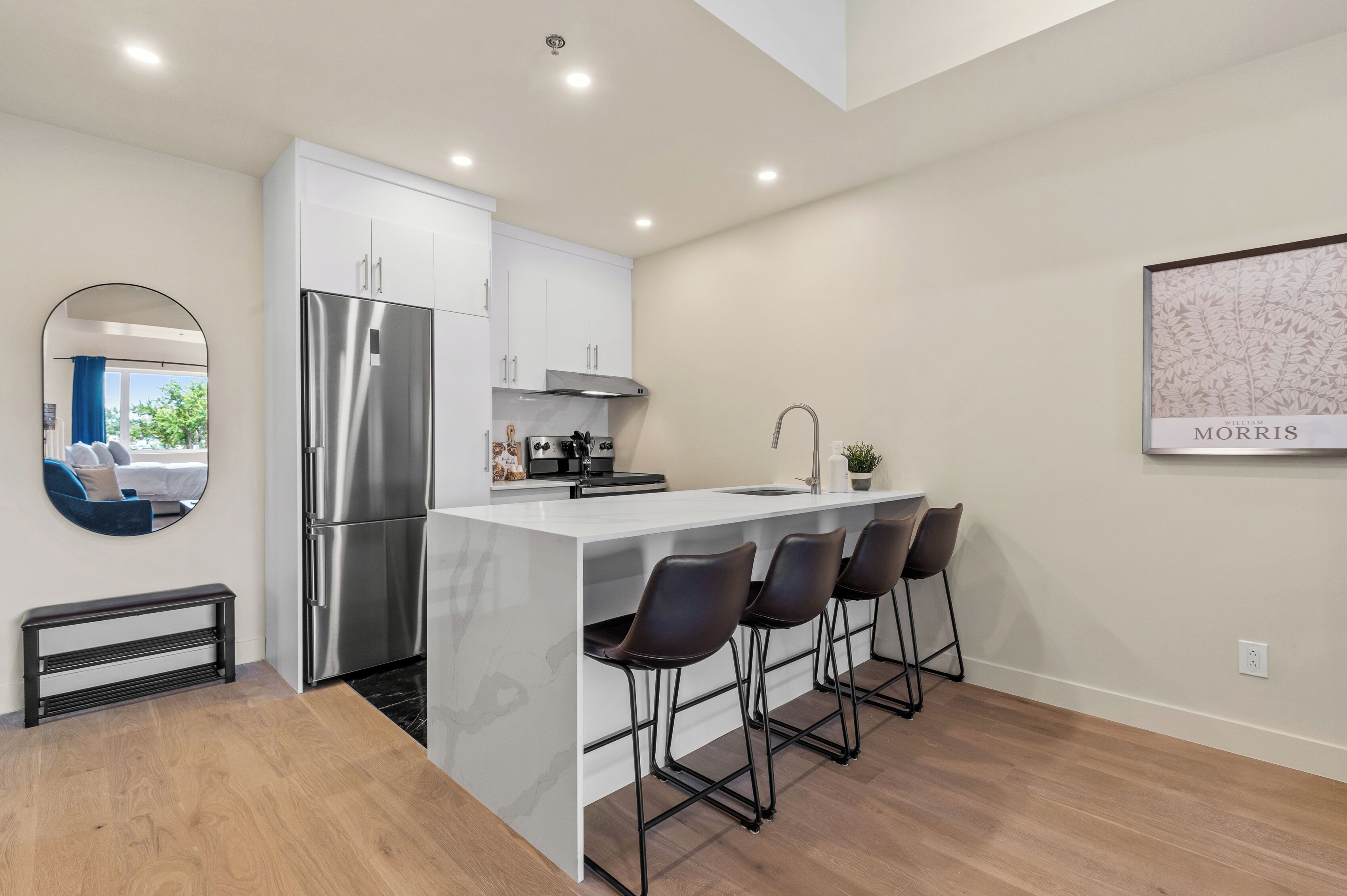 A modern kitchen with a stainless steel refrigerator, white cabinets, and a bar area with stools.