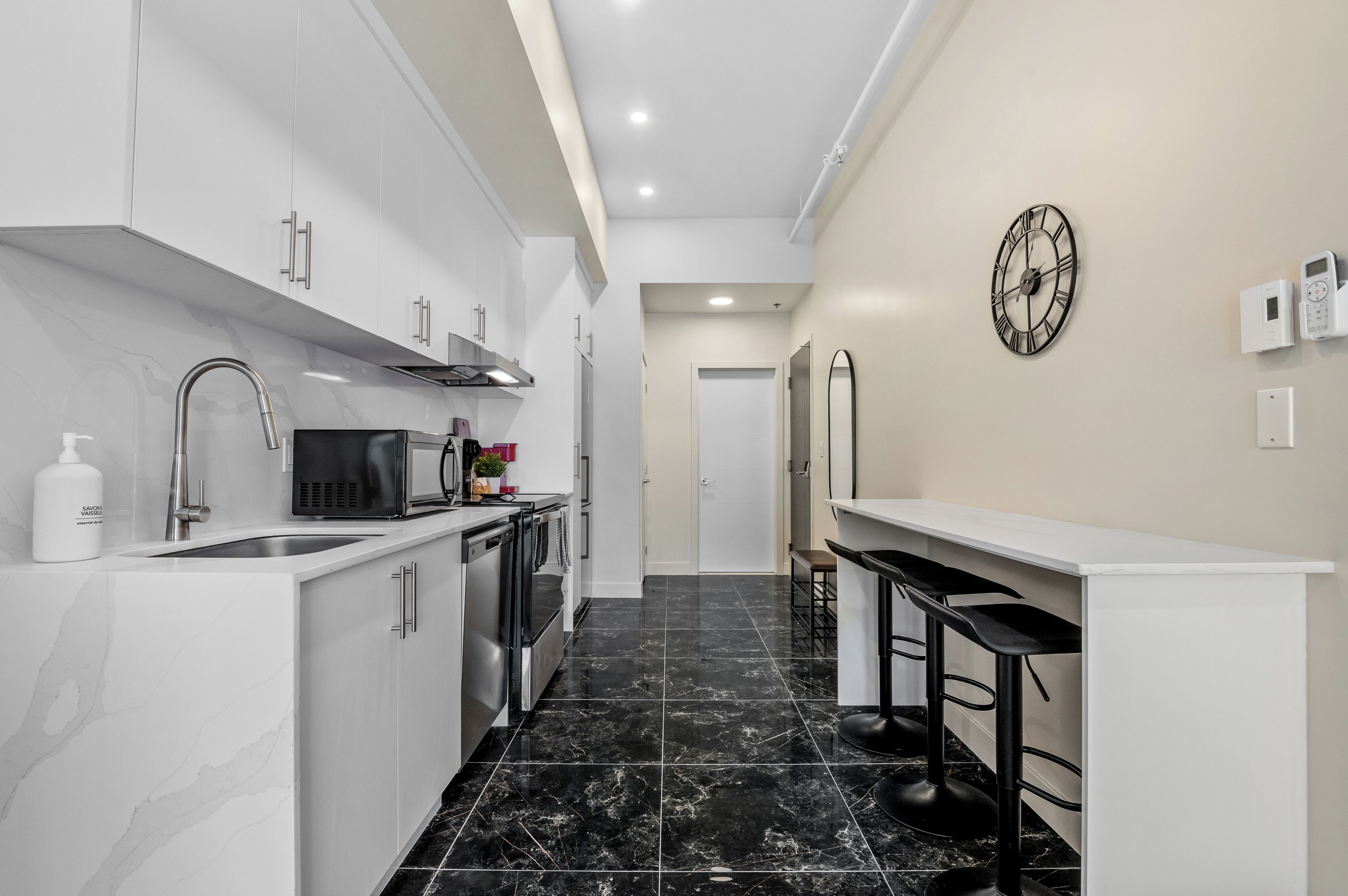 A modern kitchen with white cabinets, a black countertop, and a black tiled floor.