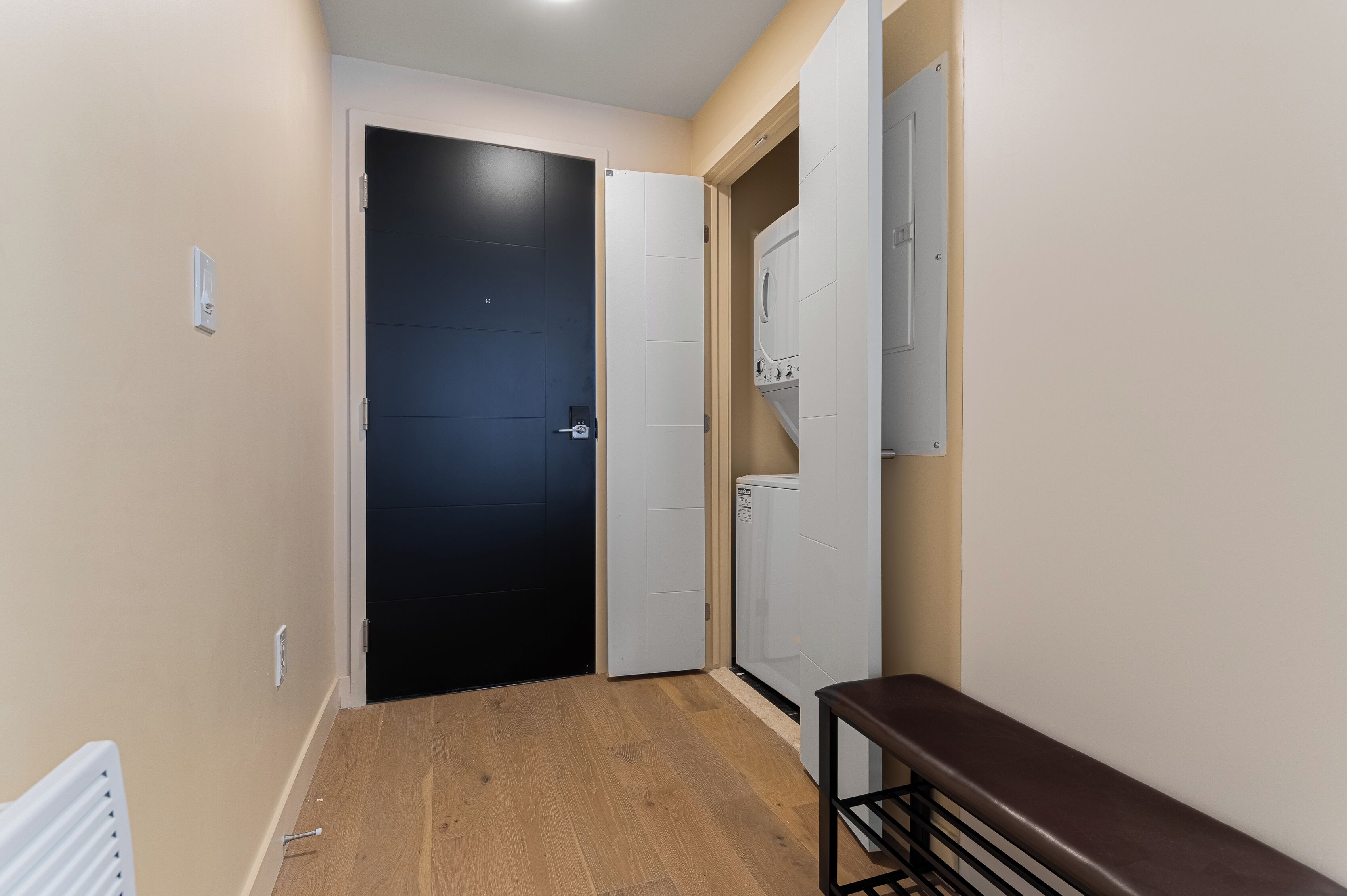 A narrow hallway with a wooden floor, a black door, and a white wall-mounted washing machine.