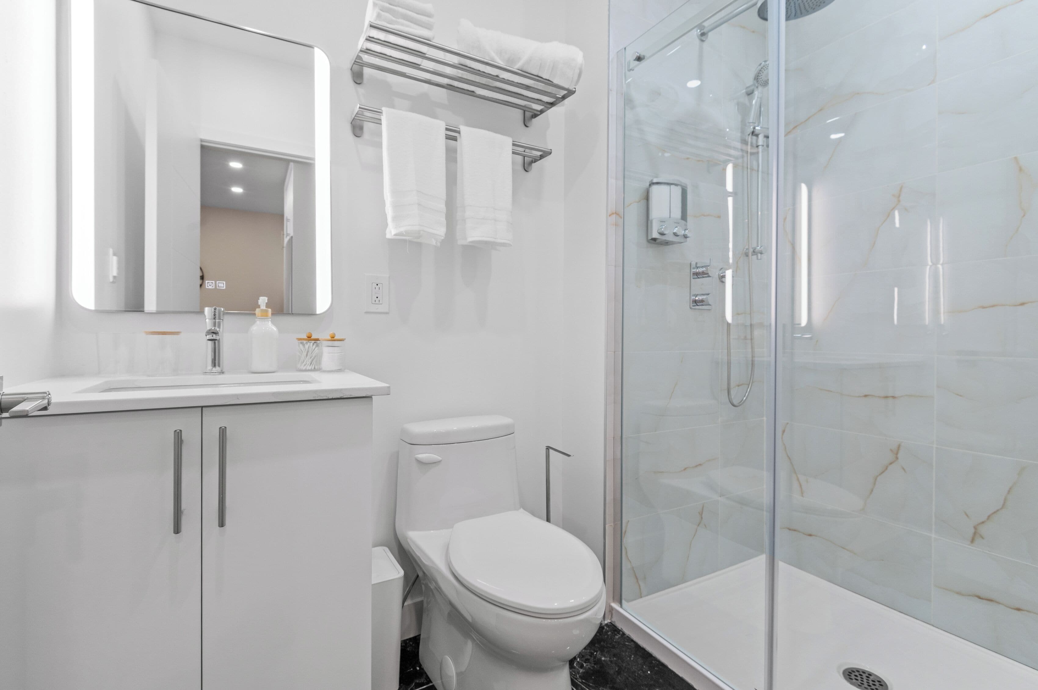 A modern bathroom with a glass-enclosed shower, a white toilet, a sink with a mirror, and a towel rack.