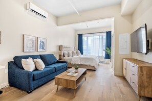 Una sala de estar moderna con un sofá azul, una mesa de centro de madera y una cama con cabecera blanca.