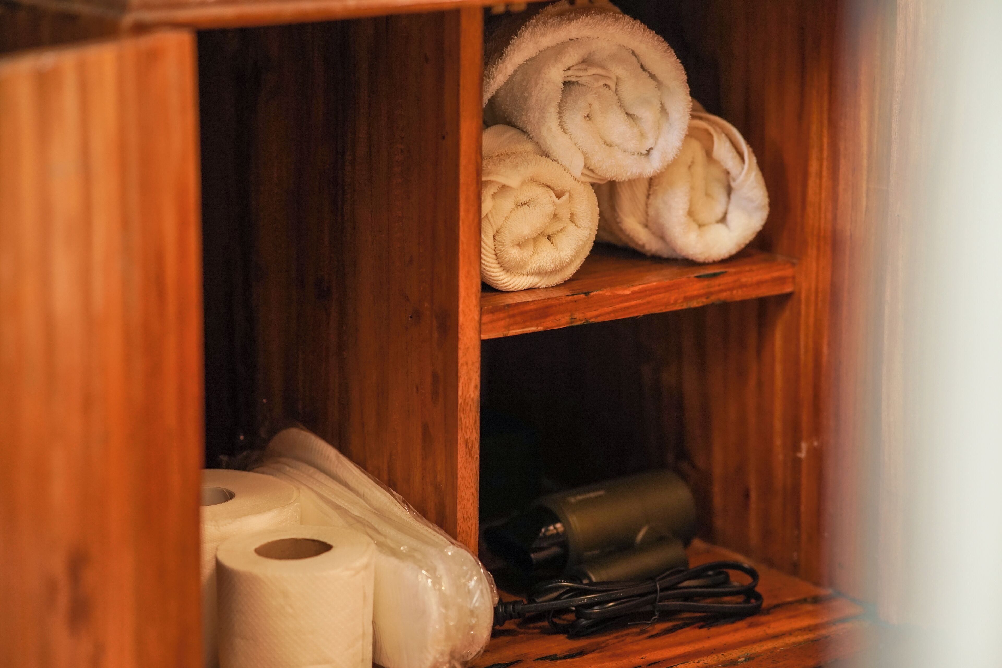 A wooden shelf with rolled towels and a roll of toilet paper.