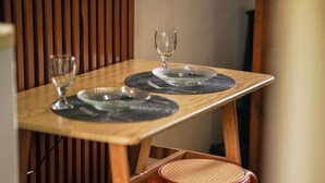 A wooden dining table with two clear glass plates, a wine glass, and woven placemats.