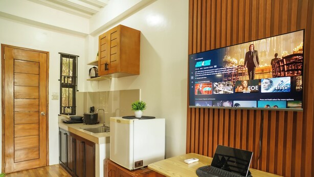 A compact kitchen with wooden cabinets, a refrigerator, and a dining area with a laptop on a table.