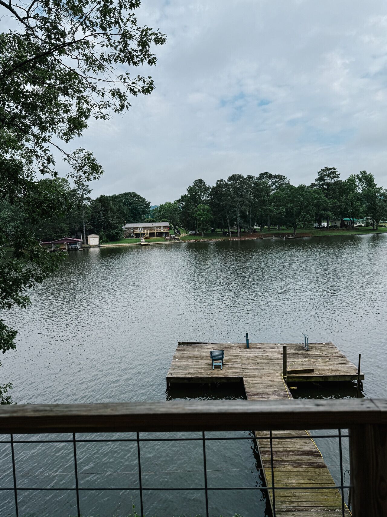 A wooden dock extending into a calm lake, surrounded by trees and a building in the background.