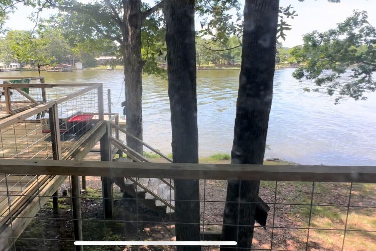A wooden dock with a metal railing overlooking a calm river, surrounded by trees.