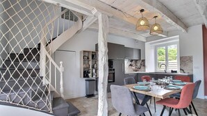A dining area with a wooden table, chairs, and a staircase with a white railing. - Villa Kercy - Plestan (PLESTAN)