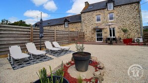 A stone building with a patio area featuring lounge chairs, a table, and a potted plant. - Villa Kercy - Plestan (PLESTAN)