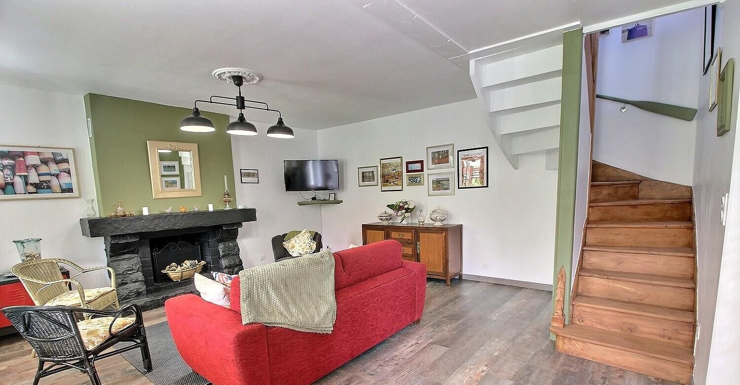Un salon avec un canapé rouge, une cheminée, un téléviseur et un escalier.