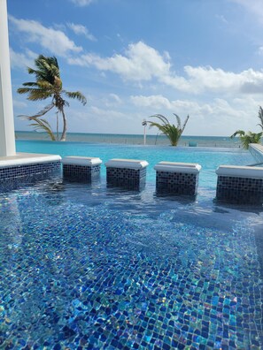 A pool with clear blue water and tiled edges, surrounded by palm trees and a view of the ocean. - Island Magic Villas (Caye Caulker)
