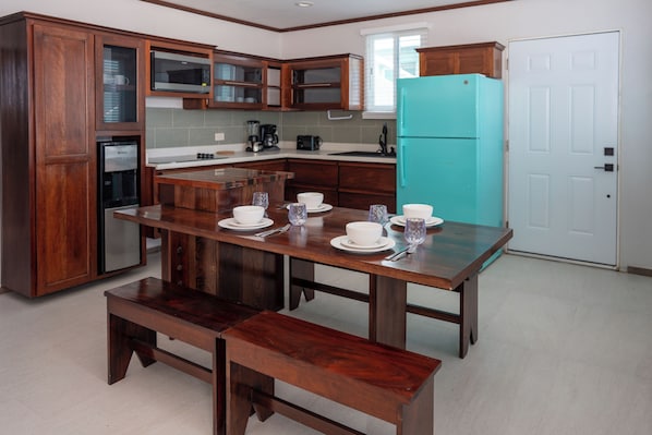 A modern kitchen with wooden cabinets, a teal refrigerator, and a dining table set for six. - Island Magic Villas (Caye Caulker)