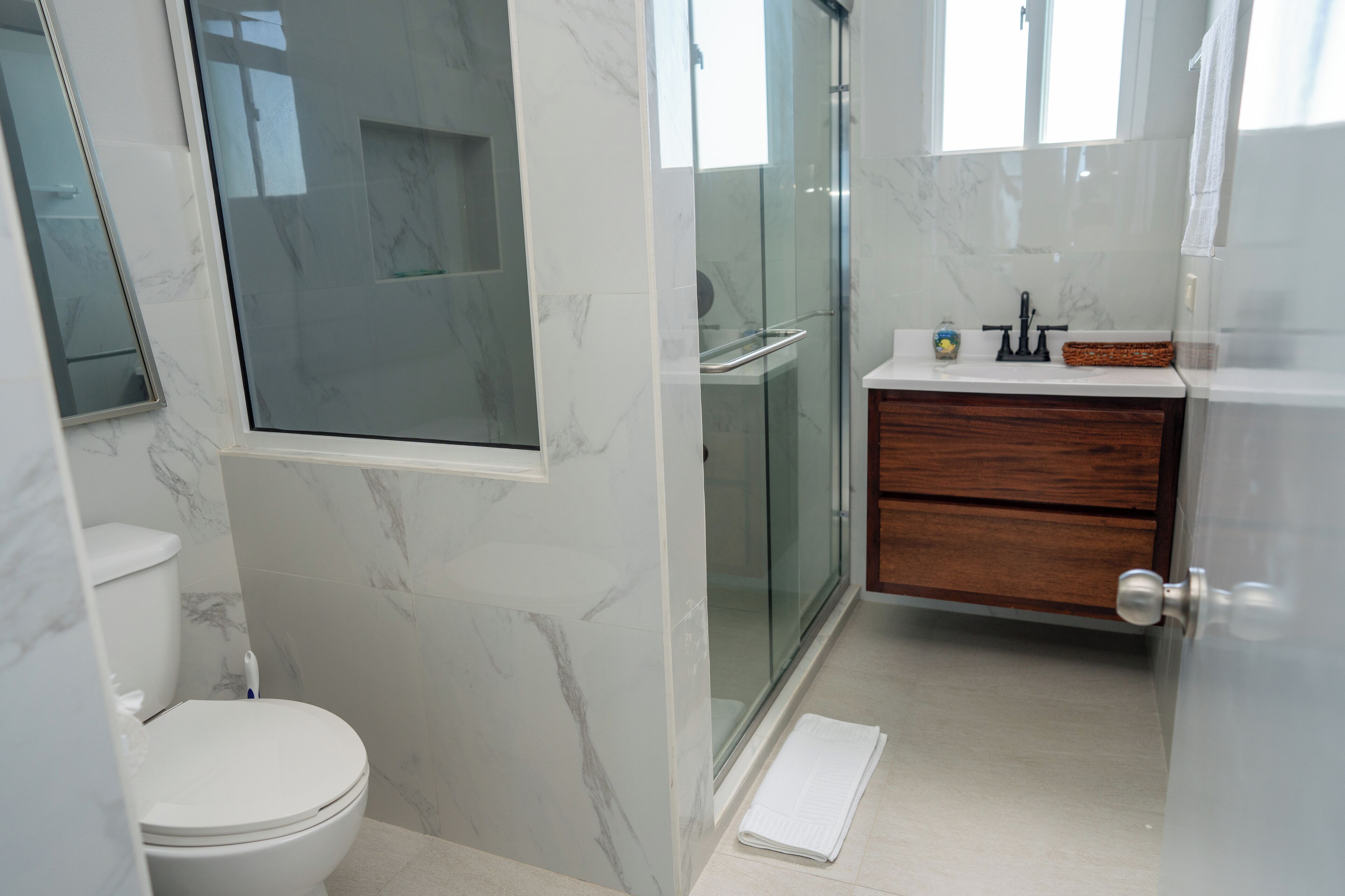 A modern bathroom with a toilet, a glass shower enclosure, a vanity with a wooden cabinet, and a marble backsplash.