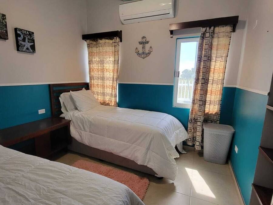 Habitación de hotel con dos camas, ventilador de techo, equipo de aire acondicionado y ventana con cortinas.