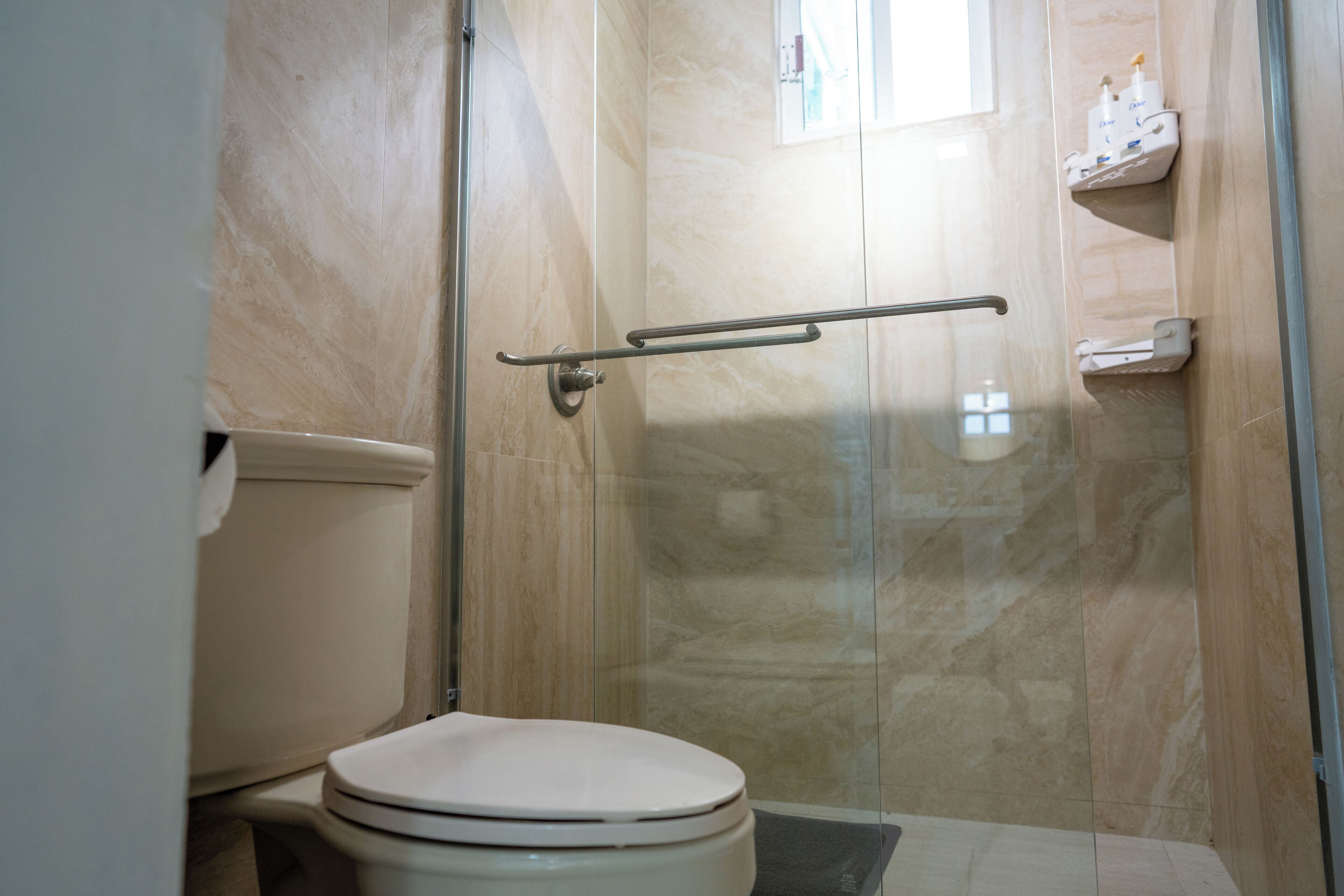 Une salle de bain équipée de toilettes, d’une douche à parois de verre et d’une étagère contenant des articles de toilette.
